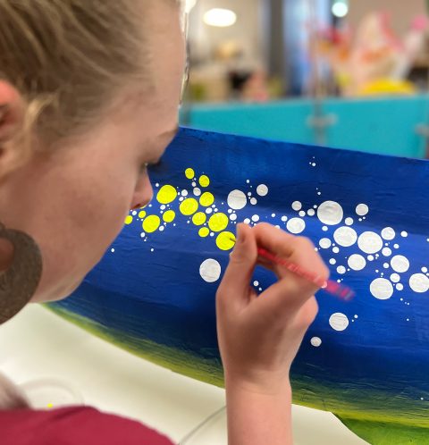 Tyler Shae painting perfect circle spots on a giant eel sculpture for blacklight instalation