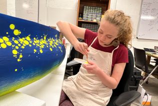 Tyler Shae painting perfect circle spots on a giant eel sculpture for blacklight instalation